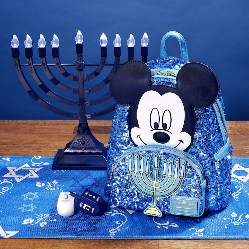 Image of our Mickey Mouse Hanukkah Mini Backpack on a Hanukkah-themed table runner with two dreidels and a menorah